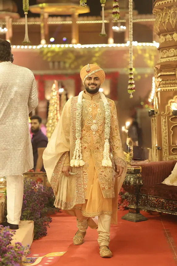 Groom walking in with floral garlands in a gold sherwani