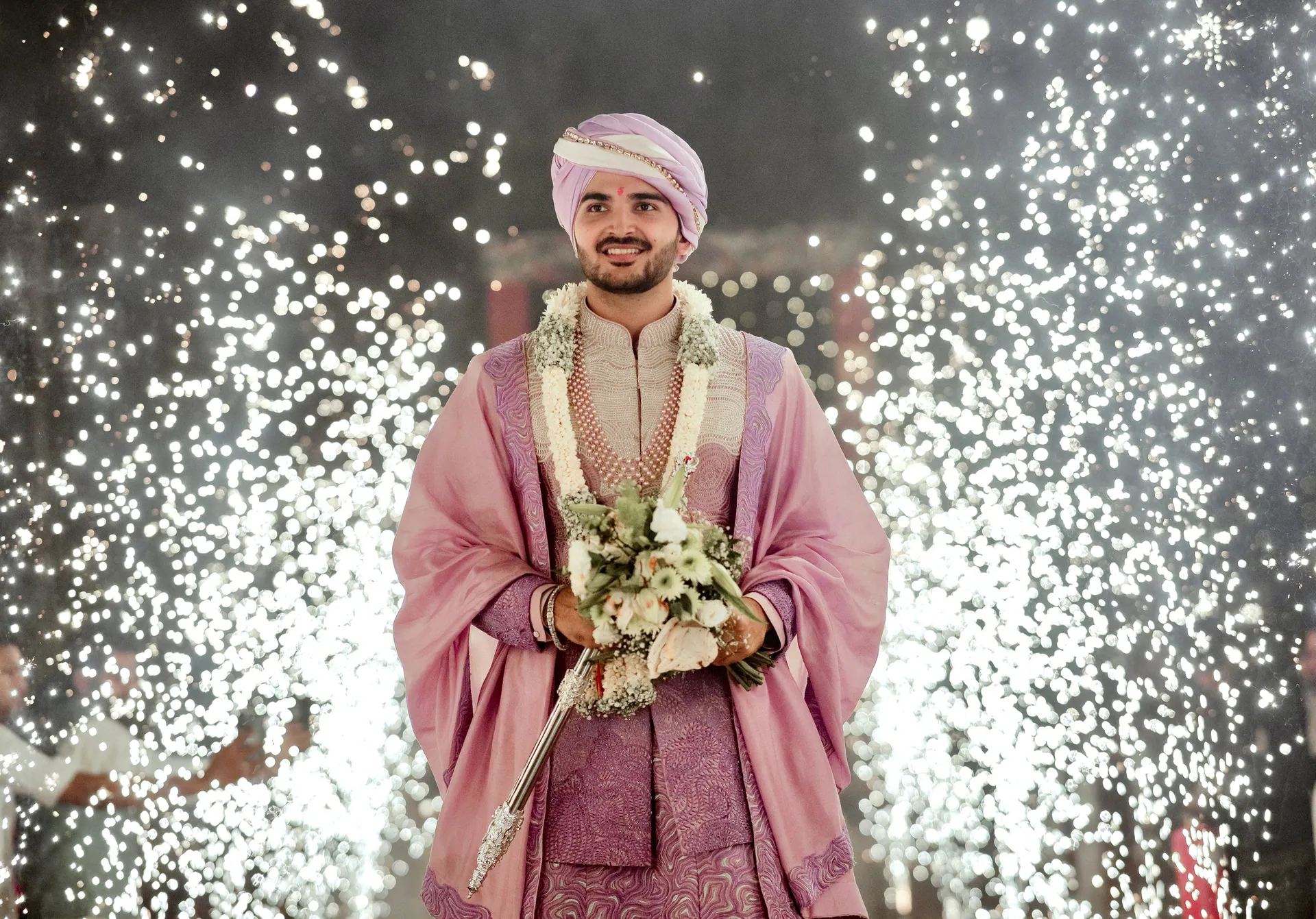Groom in a pink shawl surrounded by sparklers