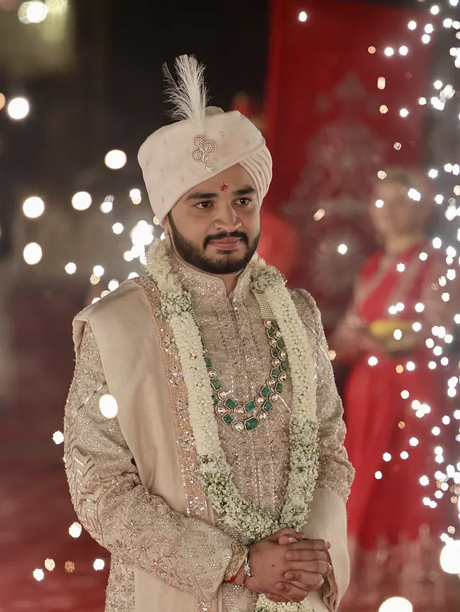 Groom in pearl-white safa with emerald mala under fairy lights